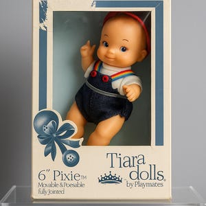 May include: A vintage 15 cm Pixie doll by Playmates, in its original box. The doll is dressed in a red cap, a white shirt with a rainbow collar, and denim overalls. The box is labelled "For Ages Over 3."