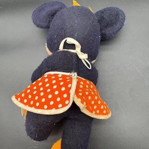 May include: A plush toy mouse wearing a red and white polka dot skirt. The mouse is black with yellow ears and feet.