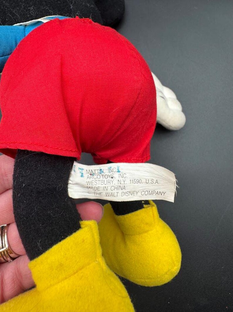 May include: A vintage Mickey Mouse plush toy, featuring red shorts, black legs, yellow shoes, and white gloves. The tag reads "MATTEL INC ARCO TOYS, INC. WESTBURY, N.Y. 11590, U.S.A. MADE IN CHINA THE WALT DISNEY COMPANY."