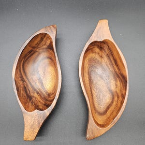 Pode incluir: Duas tigelas de madeira em forma de folha. As tigelas são feitas de madeira escura com um padrão de grão natural.
