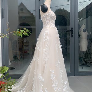 Step into your dream garden wedding with the enchanting Flower Gown, a masterpiece of elegance and bohemian charm. Imagine yourself adorned in delicate lace, flowing gracefully with every step as you make your way down the aisle. The Flower Gown is meticulously crafted to capture the essence of romance. Its intricate lace detailing exudes timeless allure, while its boho-inspired design ensures you stand out on your special day. Slip into the Flower Gown and embrace your fairy tale moment.