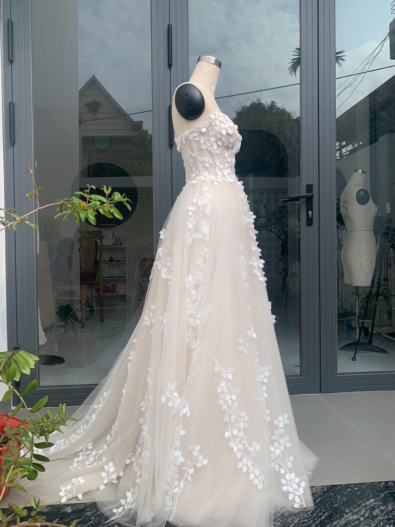Step into your dream garden wedding with the enchanting Flower Gown, a masterpiece of elegance and bohemian charm. Imagine yourself adorned in delicate lace, flowing gracefully with every step as you make your way down the aisle. The Flower Gown is meticulously crafted to capture the essence of romance. Its intricate lace detailing exudes timeless allure, while its boho-inspired design ensures you stand out on your special day. Slip into the Flower Gown and embrace your fairy tale moment.