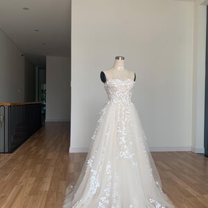 Step into your dream garden wedding with the enchanting Flower Gown, a masterpiece of elegance and bohemian charm. Imagine yourself adorned in delicate lace, flowing gracefully with every step as you make your way down the aisle. The Flower Gown is meticulously crafted to capture the essence of romance. Its intricate lace detailing exudes timeless allure, while its boho-inspired design ensures you stand out on your special day. Slip into the Flower Gown and embrace your fairy tale moment.