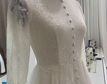 May include: A white lace dress with long sleeves and a button-up front. The dress has a fitted bodice and a flowing skirt. The dress is on a mannequin.