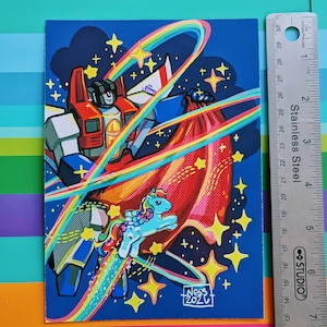 May include: A rectangular art print featuring a robot character with red, white, and blue armor holding a large red cape, accompanied by a small blue pony with a rainbow mane. The scene includes yellow stars and rainbow arcs. A metal ruler shows a height of 7 inches.