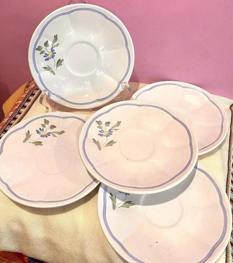 Pu&ograve; includere: Set di quattro piattini in ceramica bianca con un motivo floreale blu e verde. I piattini hanno un bordo ondulato e una fascia blu intorno al bordo.
