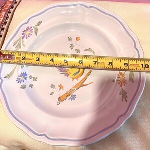 May include: A white ceramic plate with a scalloped edge and a blue border. The plate features a painted design of a yellow bird perched on a branch with flowers. The plate measures approximately 10 inches in diameter.