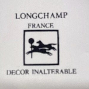 Pu&ograve; includere: Logo in bianco e nero di Longchamp Francia, con un cavallo e un cane che corrono all'interno di una cornice quadrata. Il testo "Decor Inalterable" &egrave; sotto il logo.