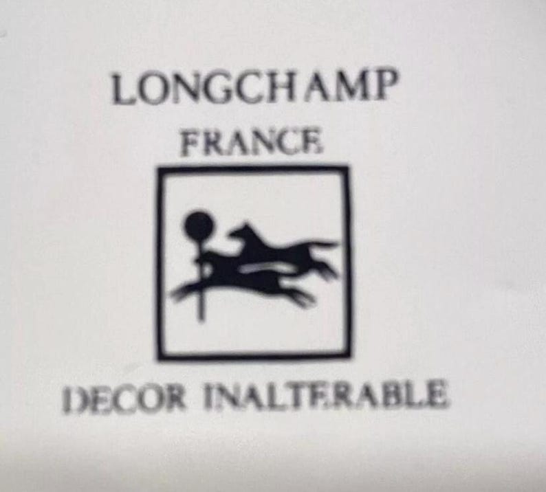 Pu&ograve; includere: Logo in bianco e nero di Longchamp Francia, con un cavallo e un cane che corrono all'interno di una cornice quadrata. Il testo "Decor Inalterable" &egrave; sotto il logo.