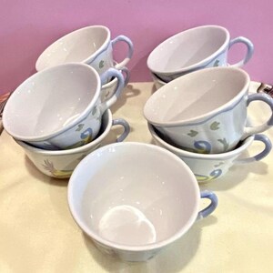 Pu&ograve; includere: Set di sei tazze da t&egrave; in ceramica bianca con motivi floreali blu e verdi. Le tazze hanno una forma arrotondata e un manico sul lato.
