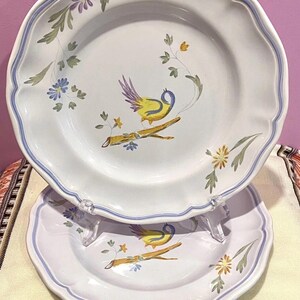 May include: Two white ceramic plates with a scalloped edge and a blue border. Each plate features a hand-painted design of a yellow bird perched on a branch, surrounded by flowers and foliage.
