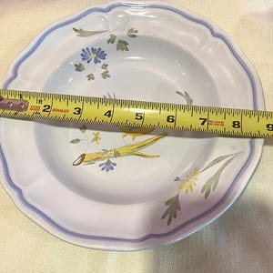 May include: White ceramic bowl with a scalloped edge and a blue and white floral design. The bowl measures approximately 8 inches in diameter. The interior features yellow and blue floral accents and green leaves.