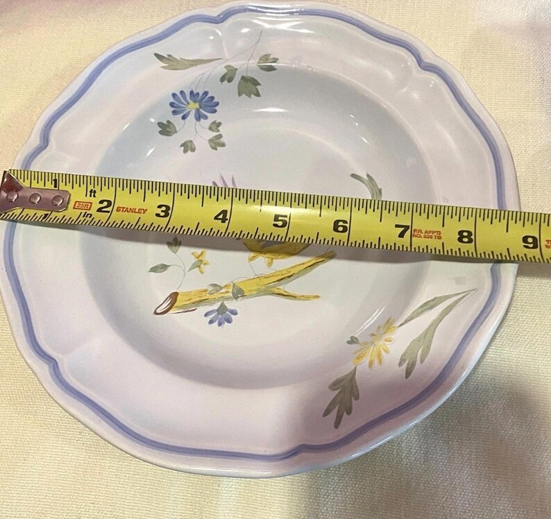 May include: White ceramic bowl with a scalloped edge and a blue and white floral design. The bowl measures approximately 8 inches in diameter. The interior features yellow and blue floral accents and green leaves.