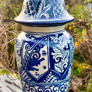 Puede incluir: Un jarrón de cerámica azul y blanco con tapa, decorado con intrincados patrones florales y geométricos. La tapa está rematada con un pináculo puntiagudo. El jarrón es probablemente para uso decorativo, con una altura de unos 30 cm.