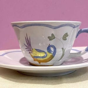 Pu&ograve; includere: Una tazza da t&egrave; e un piattino bianchi con un disegno di un uccello blu e giallo. L'uccello &egrave; appollaiato su un ramo con foglie verdi.