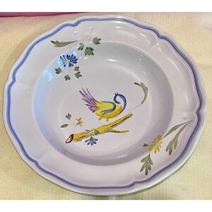 May include: White ceramic plate with a scalloped edge and a blue border. The plate features a hand-painted design of a yellow bird with purple and blue accents perched on a branch with flowers.