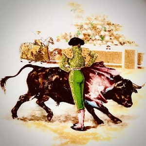 May include: A bullfighter in a green and gold suit stands in a bullring, holding a red cape. A black bull charges towards the bullfighter.