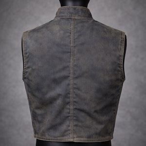 May include: A weathered-look vest in a muted gray-brown hue, displayed on a mannequin. The vest features a stand-up collar and a vertical seam down the back. The fabric has a slightly distressed appearance.