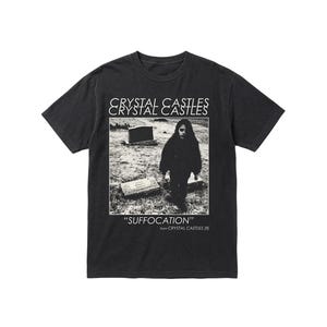 Op de afbeelding: Zwart T-shirt met een zwart-wit afbeelding van een persoon op een begraafplaats. De tekst "CRYSTAL CASTLES" staat boven de afbeelding, en "SUFFOCATION" eronder, met "from CRYSTAL CASTLES (II)" eronder. Het shirt is donker van kleur.