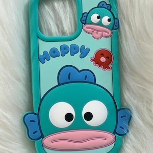 May include: A turquoise blue phone case with a cartoon fish design. The fish has big eyes, a pink mouth, and blue fins. The case also has the word "Happy" written on it in a playful font.