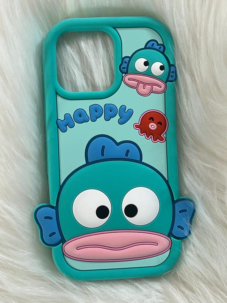 May include: A turquoise blue phone case with a cartoon fish design. The fish has big eyes, a pink mouth, and blue fins. The case also has the word "Happy" written on it in a playful font.