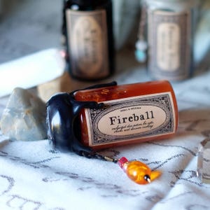 May include: A small, orange "Fireball" potion bottle with a black wax seal and a decorative charm. The label reads "Fireball enchanted dice potion for rolls, checks, and decision making."