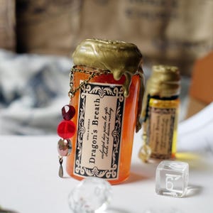 May include: An orange potion bottle with a gold wax seal and a decorative chain with red and clear beads. The label reads "Dragon's Breath" and "enchanted dice potion for rolls, checks and decision making."