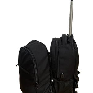 May include: Black rolling backpack with a telescopic handle. The backpack has two large compartments and multiple pockets.