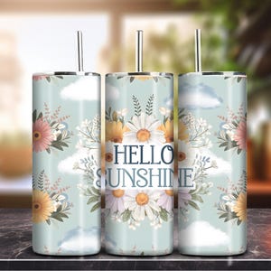 Puede incluir: Tres vasos de acero inoxidable con tapas y pajitas. Los vasos están decorados con un patrón floral y el texto "Hello Sunshine".