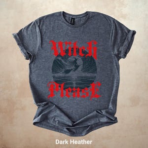 May include: Dark heather gray t-shirt with the text "Witch Please" in red gothic lettering. The shirt features a circular graphic of a witch flying over water. The shirt is made of a soft material.