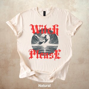 May include: A natural-colored t-shirt featuring a graphic design with the words "Witch Please" in red gothic lettering. The design includes a witch on a broomstick flying in front of a dark circle. The word "Natural" is printed at the bottom.