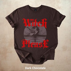 May include: Dark chocolate-colored t-shirt with rolled-up sleeves. The shirt features a red gothic font design that reads "Witch Please" above and below a gray illustration of a witch flying over water. The text "Dark Chocolate" is at the bottom.