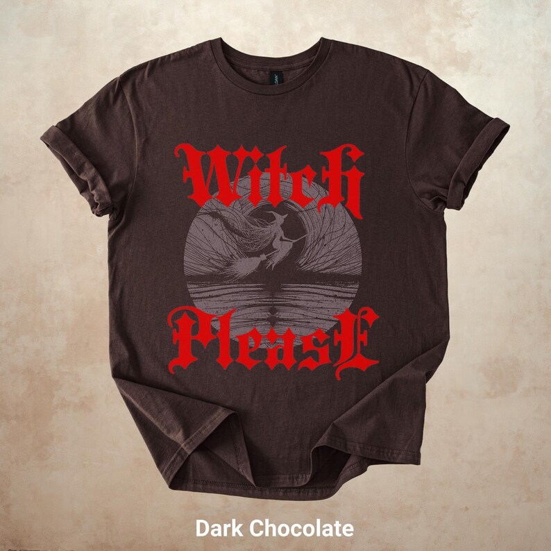 May include: Dark chocolate-colored t-shirt with rolled-up sleeves. The shirt features a red gothic font design that reads "Witch Please" above and below a gray illustration of a witch flying over water. The text "Dark Chocolate" is at the bottom.