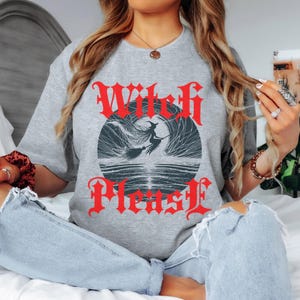 May include: A heather gray t-shirt with the words "Witch Please" in red gothic lettering. The shirt features a graphic of a witch flying on a broomstick in front of a full moon.