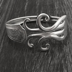 May include: Silver spoon bracelet with a decorative swirl design. The bracelet is made from a recycled spoon and has a unique, handmade look.