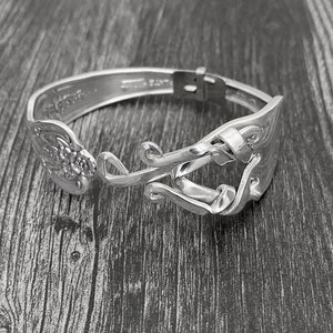 Peut inclure: Un bracelet en argent fait à partir d'une cuillère décorée d'un motif floral. Le bracelet est fabriqué à partir d'une cuillère recyclée et a un aspect unique et artisanal.