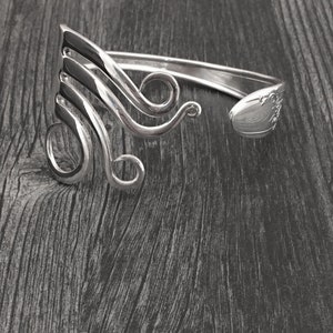 May include: A silver bracelet made from a repurposed fork, with a swirling design.