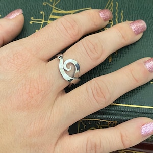 May include: A silver ring with a swirl design. The ring is worn on a finger.
