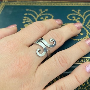 May include: A silver ring with a unique, swirling design. The ring is made of metal and has a hammered texture.