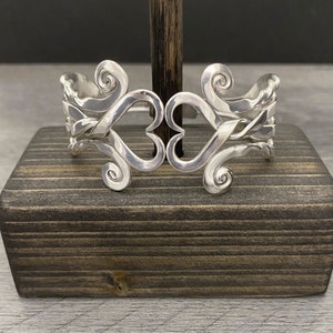 May include: Silver bracelet with a heart design and swirling details. The bracelet is made of multiple strands of silver that are intertwined to create a unique and intricate design.