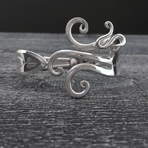 May include: Silver bracelet made from a recycled spoon, featuring a swirling, ornate design.
