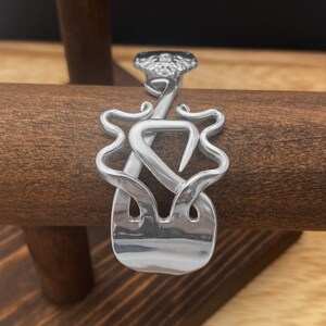 May include: A silver bracelet made from a repurposed fork, shaped into a decorative design.