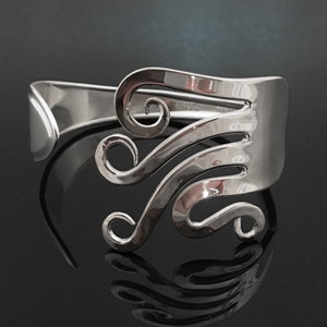 May include: A silver bracelet made from a repurposed fork, with the tines bent into a swirling design.