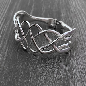 May include: A silver bangle bracelet with a Celtic knot design. The bracelet is open and has a hinged clasp.