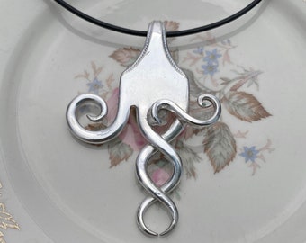 Puede incluir: Un collar de plata con un colgante hecho de un tenedor reutilizado. El colgante tiene la forma de un pulpo estilizado con tentáculos en espiral.