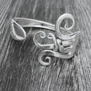 May include: A silver bracelet made from a recycled fork, with a decorative design of swirls and loops.