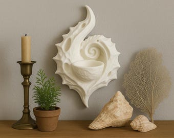 May include: A decorative wall-mounted candle holder with a seashell design, a brass candlestick with a beige candle, a small potted plant, and seashells. The items are arranged on a wooden surface against a gray wall.
