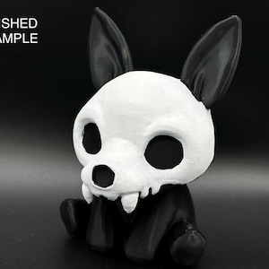 May include: A small, black and white figurine of a dog with a skull-like face. The dog has large, black eyes and a toothy grin.