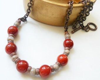 May include: A copper chain necklace with red and gray beads. The necklace has a lobster clasp and a decorative ring.