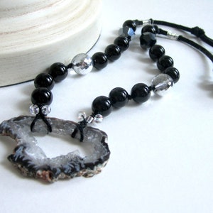May include: A black and silver beaded necklace with a large, gray agate pendant. The pendant has a natural, rough-hewn edge and a hole in the center.